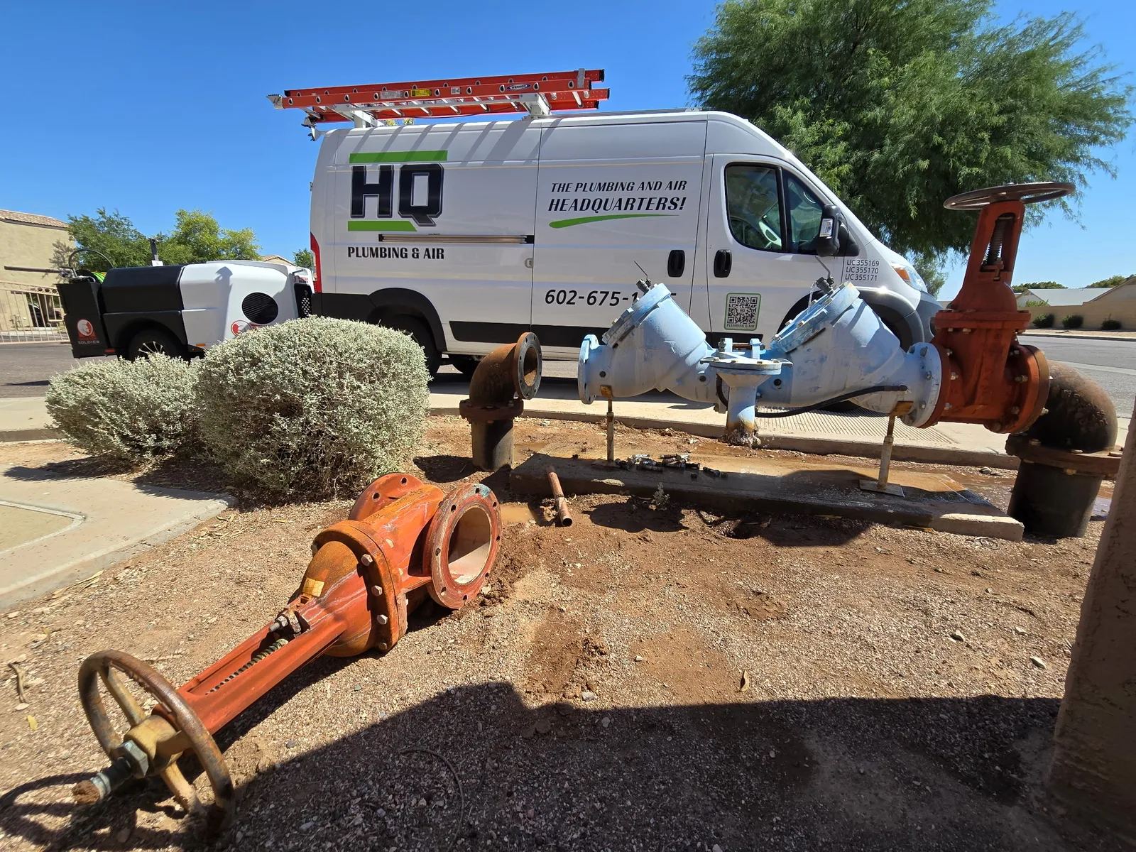 HQ Plumbing van beside a commercial backflow and gate valve assembly on a Phoenix sewer job